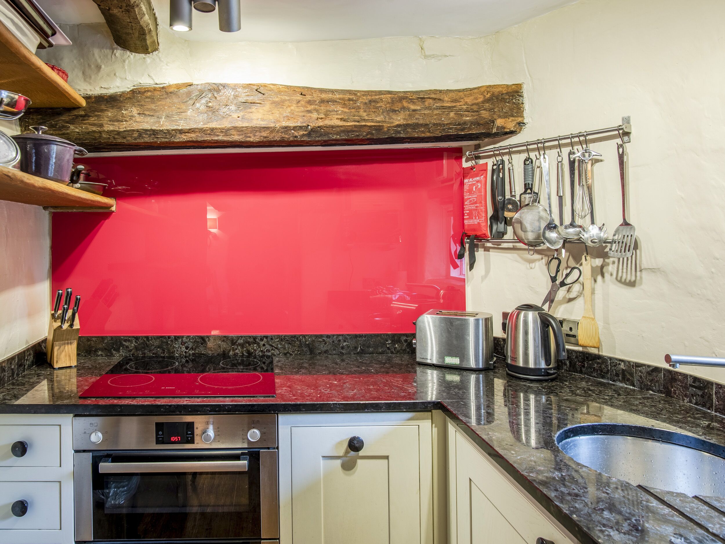 A kitchen with a red backsplash, stainless steel appliances, and a hanging utensil rack.