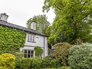A white building with a stone chimney, surrounded by lush greenery and trees. - Knotts Cottage (Windermere)