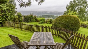 Eine Holzterrasse mit Tisch und Stühlen, umgeben von einem Holzzaun und üppiger Bepflanzung.
