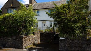 A traditional stone house with a white exterior, a thatched roof, and a small garden with a fountain. - Uldale (Ambleside)
