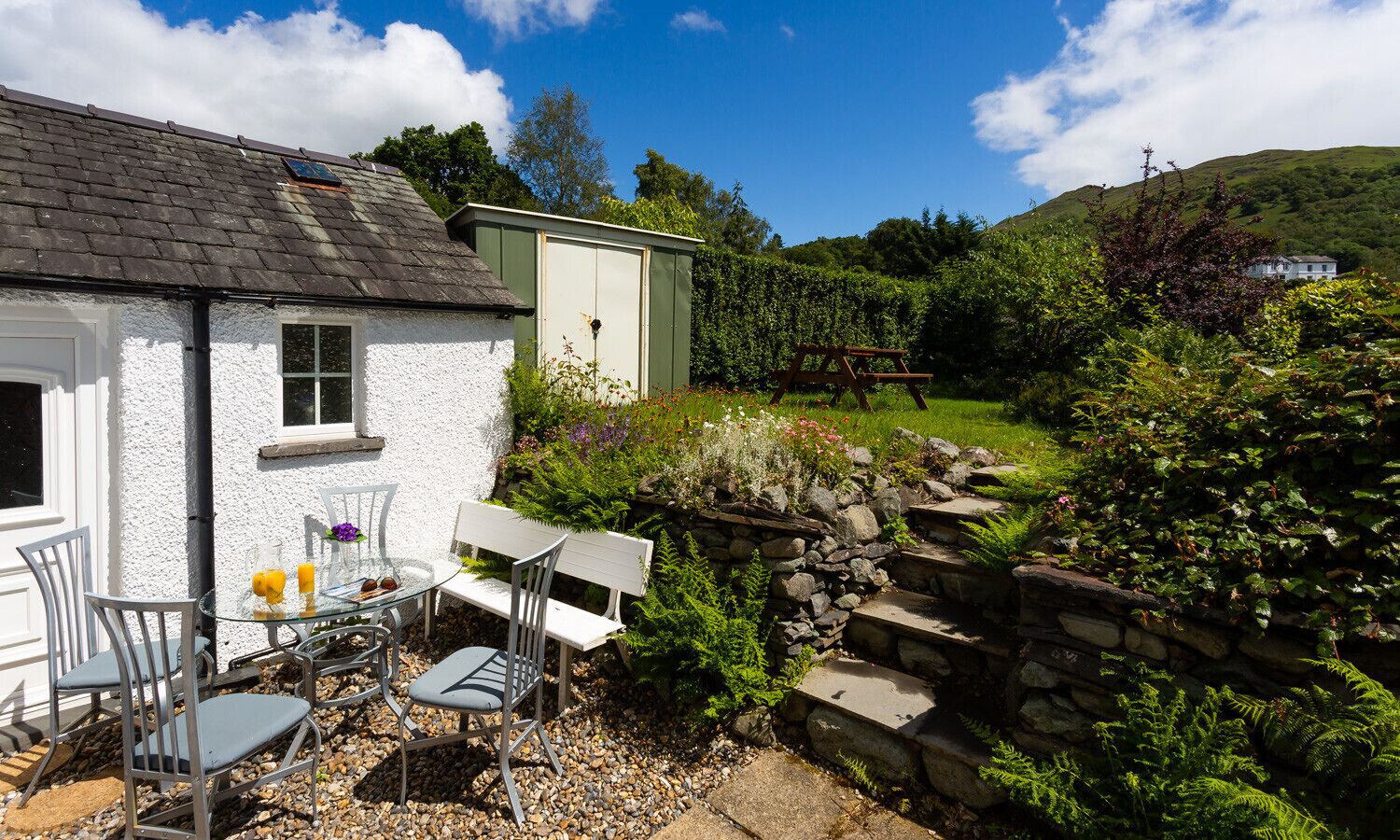 A white house with a garden, a stone wall, and a picnic table.