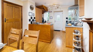A kitchen with wooden cabinets, a central island, and a white door. - Uldale (Ambleside)