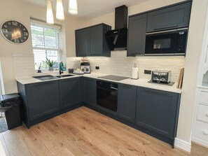 A modern kitchen with dark cabinetry, a built-in oven, a microwave, and a toaster. - Newby Bridge House (Ulverston)