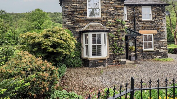 A stone house with a gabled roof, a bay window, and a small porch. - Newby Bridge House (Ulverston)