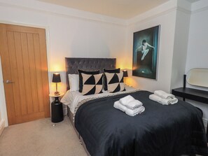 A bedroom with a bed, two bedside lamps, a door, a framed picture on the wall, and a small table with towels. - Newby Bridge House (Ulverston)