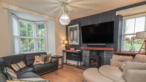 A living room with a sofa, armchair, fireplace, TV, and a chandelier. - Newby Bridge House (Ulverston)