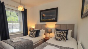 A hotel room with two beds, a window with curtains, a framed picture on the wall, and a lamp on each nightstand. - Newby Bridge House (Ulverston)