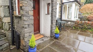 A stone building with a red door, a small porch, and two potted plants. - Hideaway Cottage (Ambleside)