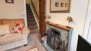 A living room with a sofa, fireplace, and a staircase. - Hideaway Cottage (Ambleside)