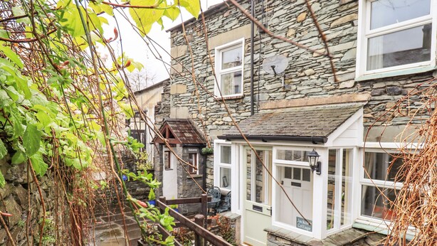A stone cottage with a small garden, a wooden fence, and a narrow water channel. - Hideaway Cottage (Ambleside)