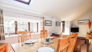 A dining area with a wooden table set for four, a sofa, and a television in a living room. - Spring Cottage (Ambleside)