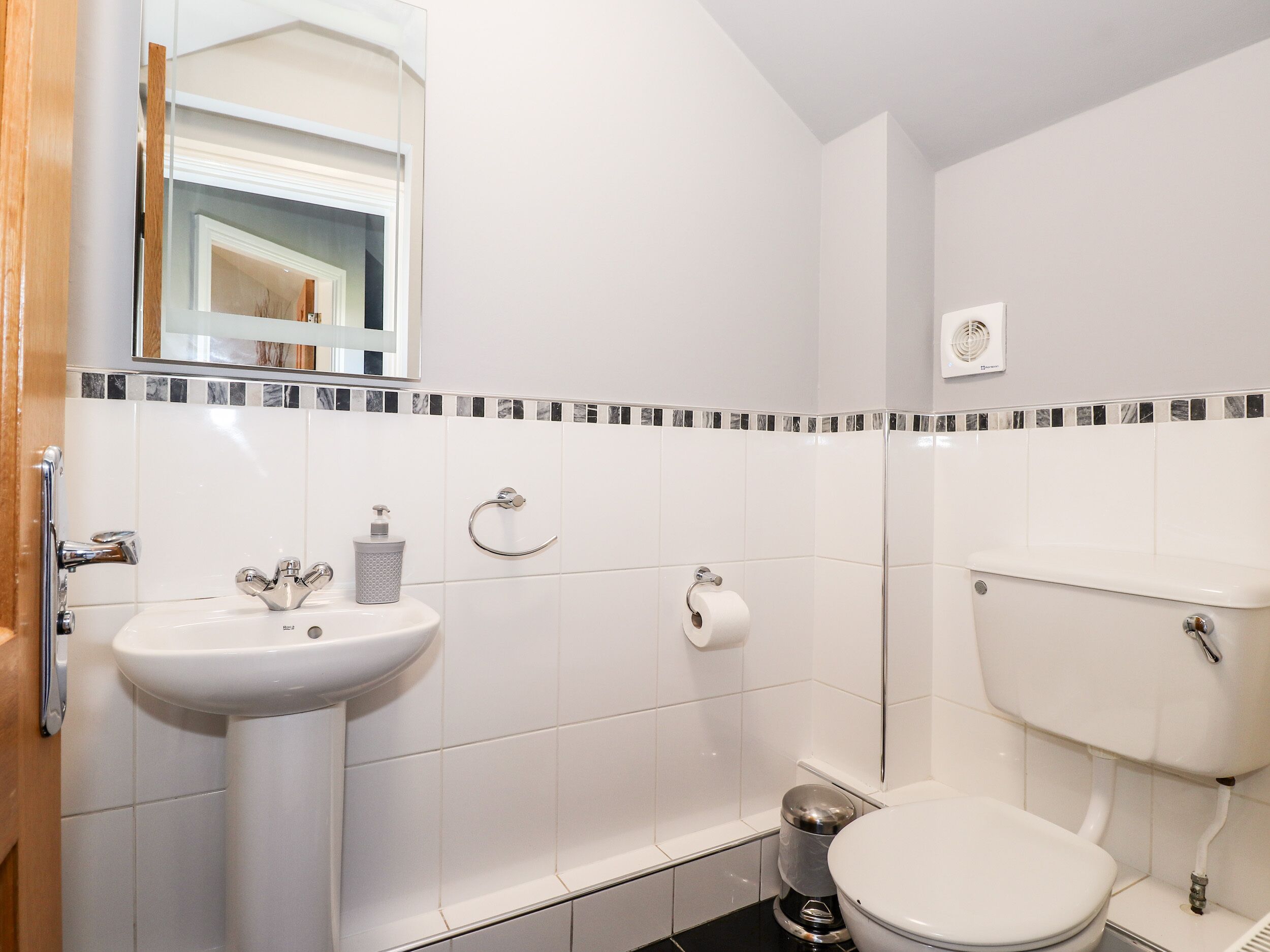 Une salle de bain avec un lavabo, des toilettes et un miroir, le tout de couleur blanche.