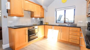 A modern kitchen with wooden cabinets, a built-in oven, and a window providing a view of the outdoors. - Spring Cottage (Ambleside)