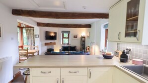 A modern kitchen with light-colored cabinets, a wooden beam ceiling, and a dining area with a sofa and table. - Drystones (Ambleside)