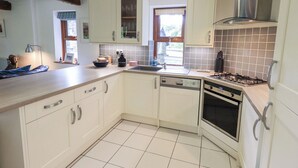 A kitchen with white cabinets, a dishwasher, a stove, and a window with curtains. - Drystones (Ambleside)