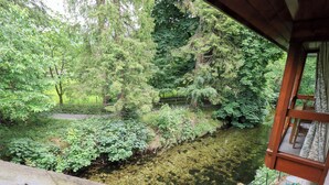 A view of a lush green landscape with a clear stream, a wooden deck, and a stone ledge. - Drystones (Ambleside)