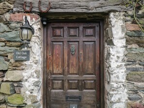 Une porte en bois rustique, sur laquelle on peut lire l’inscription « Old Oak Cottage », et un mur de pierres surmonté d’une lanterne.