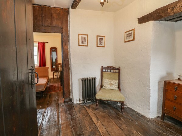 Une pièce avec un plancher en bois, un fauteuil ancien, un radiateur et un meuble en bois.