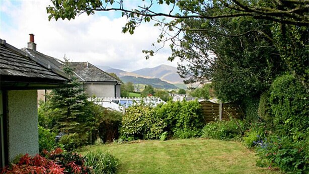 A garden with a lawn, various shrubs, and a house with a sloped roof.