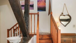 Un escalier avec des rampes en bois, un lavabo blanc et un miroir avec un cadre en forme de cœur.
