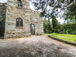 A stone building with a gravel driveway, a bench, and a garden area.