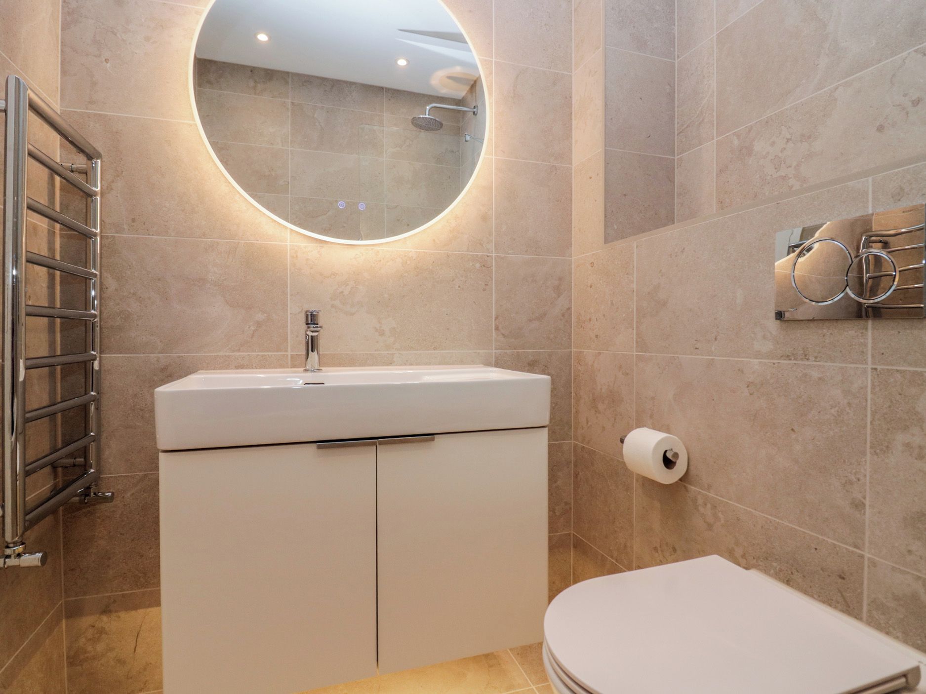 Une salle de bain moderne avec un miroir rond, un lavabo blanc, des toilettes et un porte-serviettes.