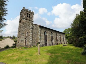 A stone church with a bell tower, arched windows, and a grassy lawn.