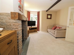 A living room with a stone fireplace, a television on a wooden stand, a beige sofa, and a door.