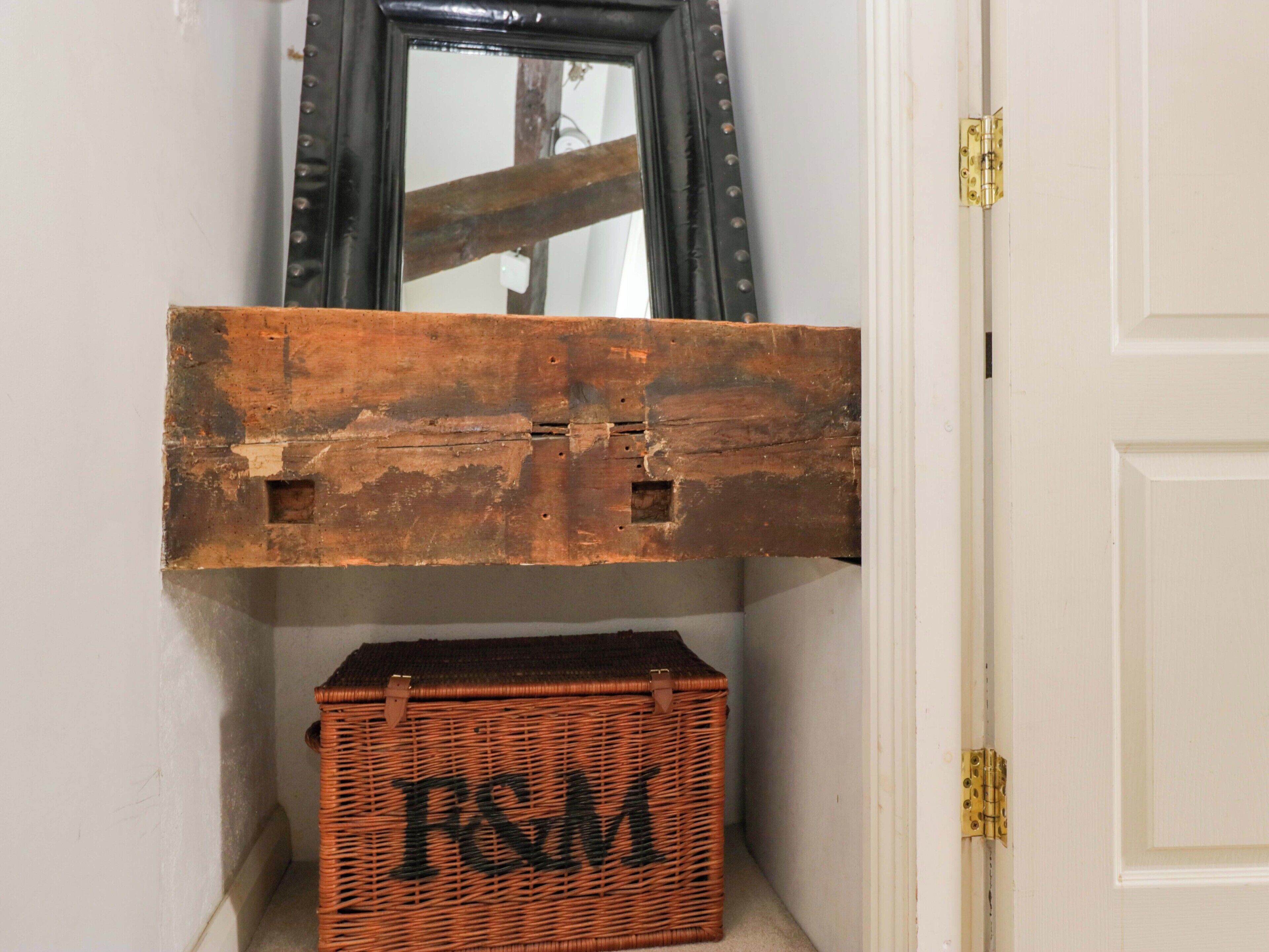 A rustic wooden chest with a metal clasp, a wicker basket with 'F&M' branding, and a mirror above.