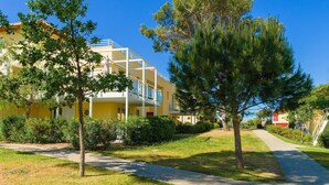A yellow building with balconies, surrounded by trees and a pathway.