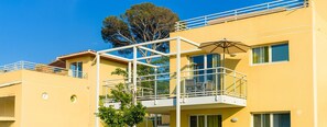 Un edificio amarillo con balcón, un árbol y un cielo azul despejado.