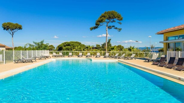 Una piscina rectangular con agua cristalina, rodeada de sillas de descanso y una valla.