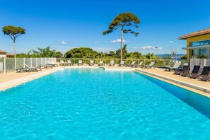 Una piscina rectangular con agua cristalina, rodeada de sillas de descanso y una valla.