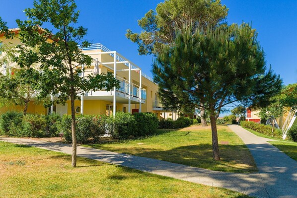 Un edificio amarillo con balcones, rodeado de árboles y un sendero.
