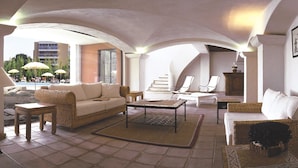 A spacious living room with a high ceiling, a view of the pool area, and a seating arrangement including a sofa, chairs, and a coffee table.