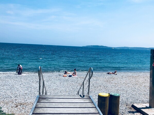A wooden jetty leading to a pebble beach with a view of the sea and distant hills.