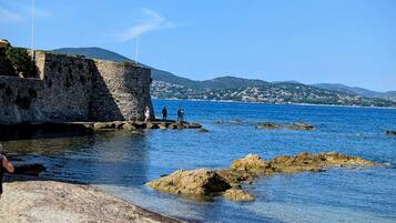 Une plage côtière bordée d’une eau bleue et limpide, de formations rocheuses et d’un mur de pierres.