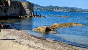 A coastal beach with clear blue water, rocky outcrops, and a stone wall.