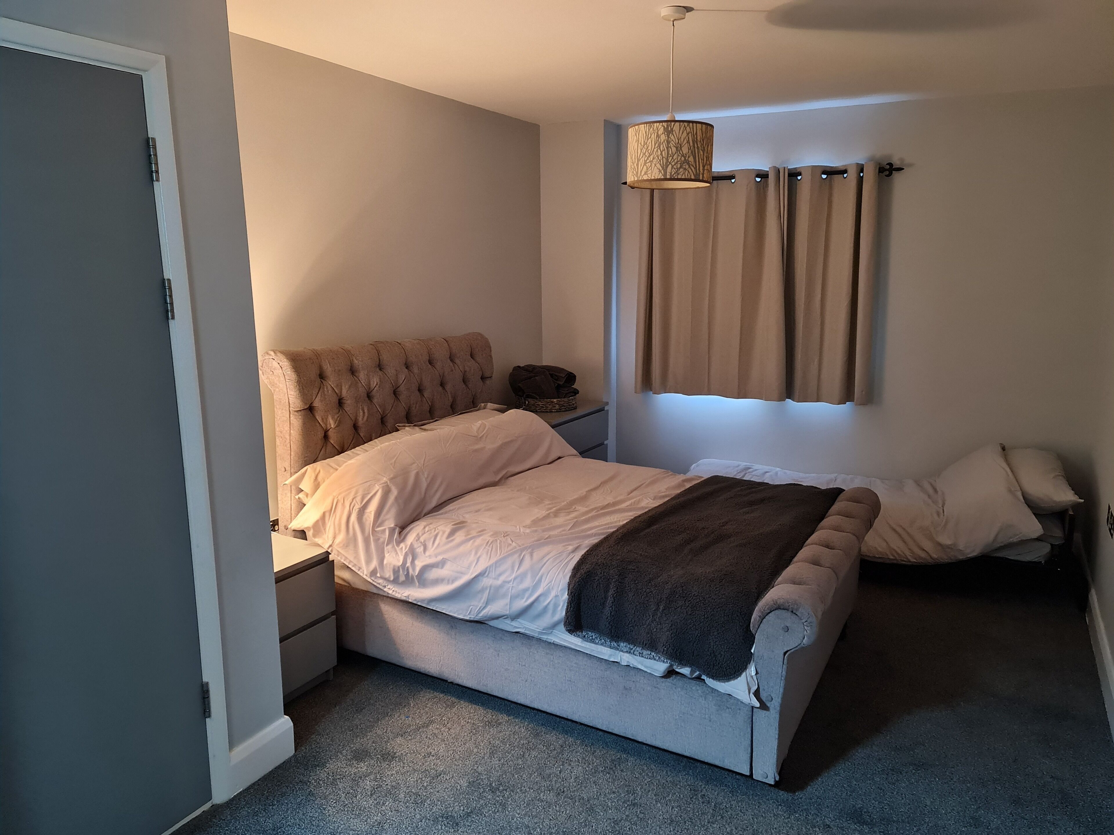 A bedroom with a bed, a bedside table, a lamp, and a window with curtains.