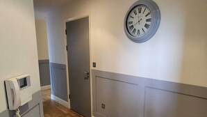 A hallway with a wooden floor, a door, and a wall-mounted clock. - Stunning 3-bed Apartment in Heart of Cardiff Bay (Cardiff)