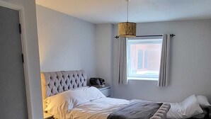 A bedroom with a large bed, a bedside table, a nightstand, a hanging lamp, and a window with curtains. - Stunning 3-bed Apartment in Heart of Cardiff Bay (Cardiff)