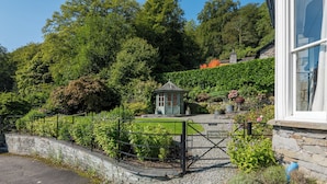 A garden with a gazebo, stone wall, and a gravel path leading to a gate.