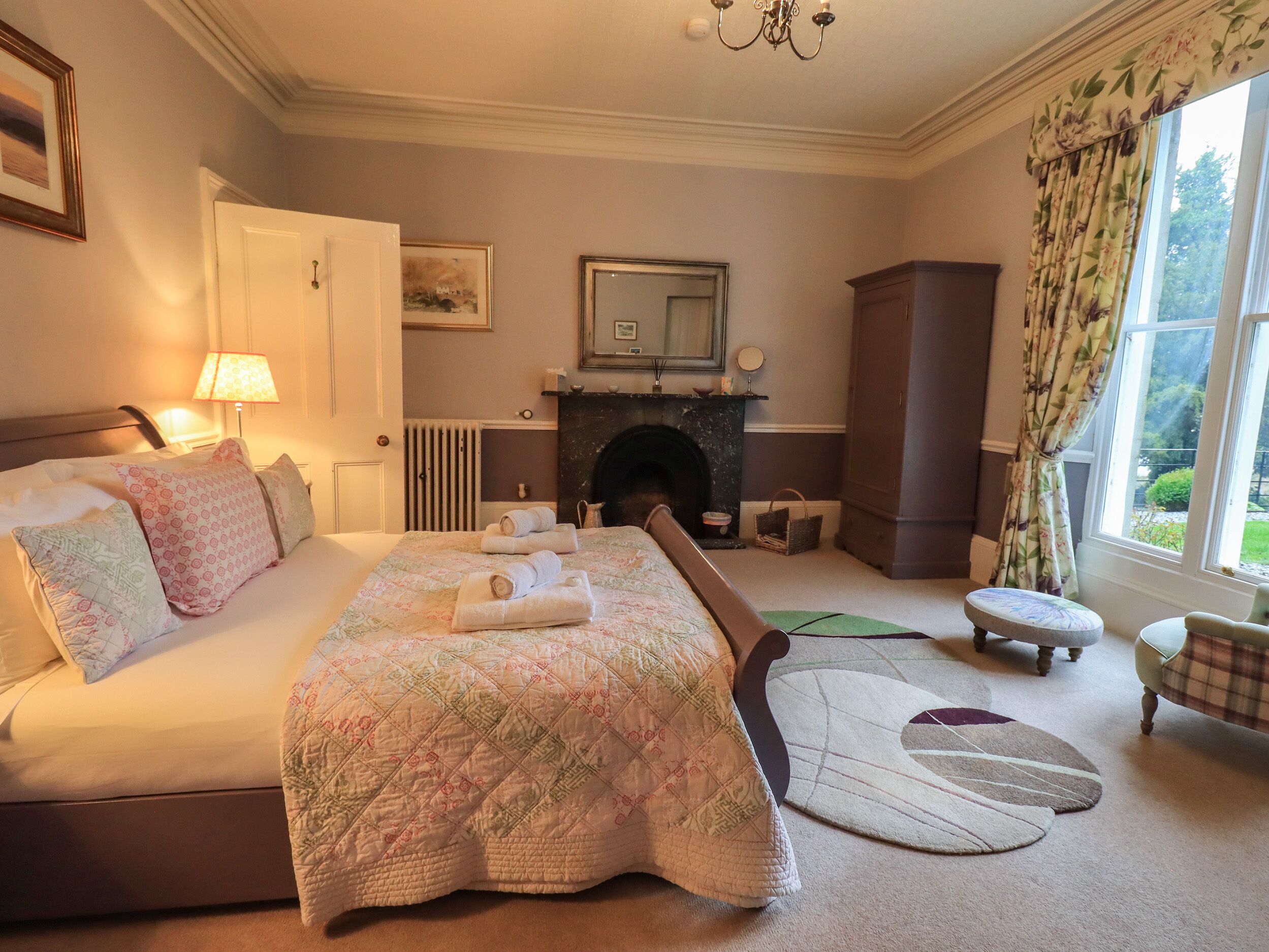 A well-appointed bedroom with a large bed, a fireplace, a sitting area, and a view of the outdoors.