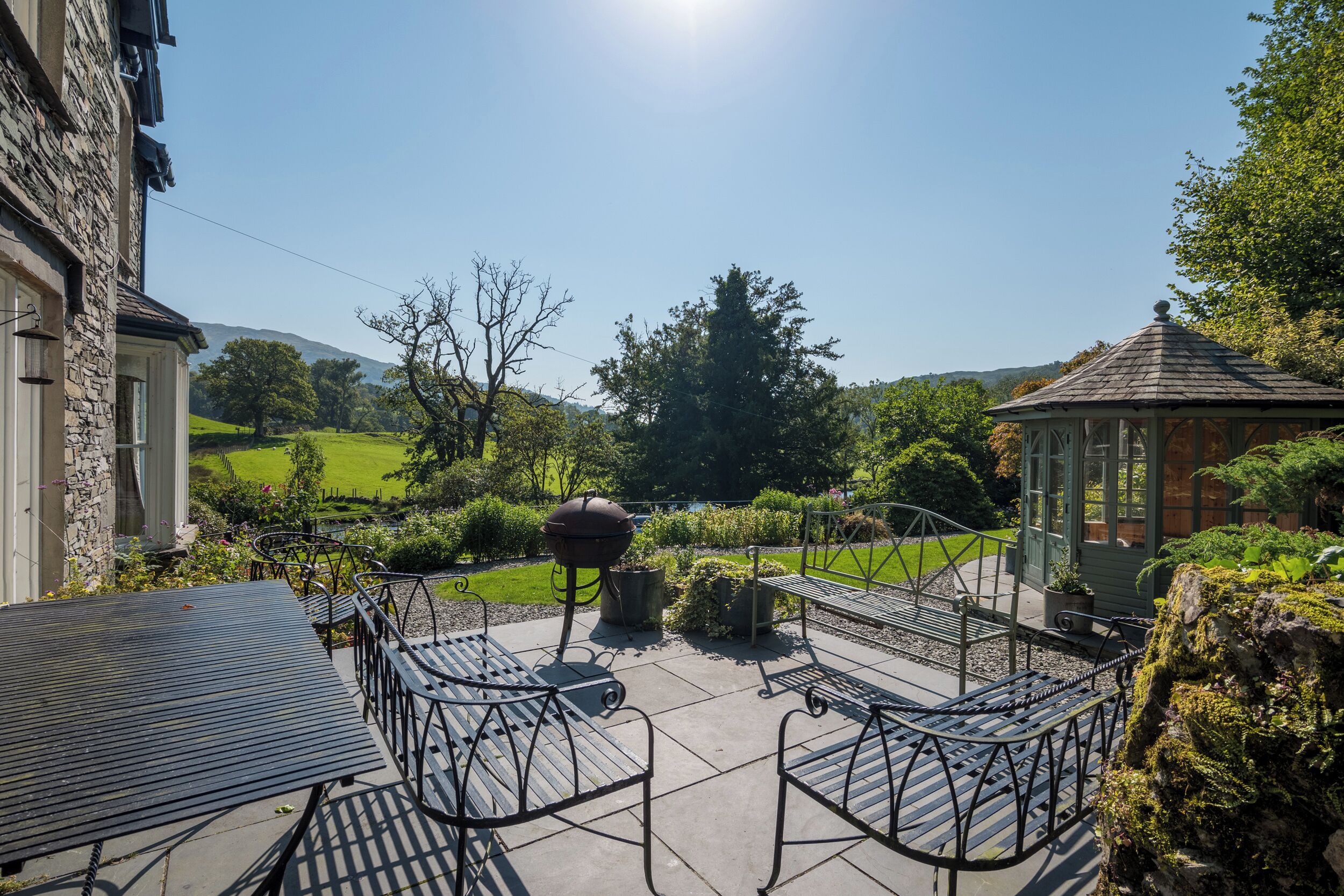 A patio with metal chairs and a table, surrounded by greenery and a gazebo.