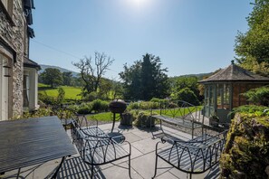 Eine Terrasse mit Metallstühlen und einem Tisch, umgeben von Grünpflanzen und einem Pavillon.