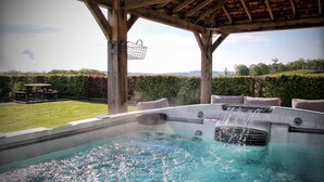 A hot tub with a waterfall feature, surrounded by a wooden pergola, a picnic table, and a well-maintained lawn. - Hawkrigg Farm (Ambleside)