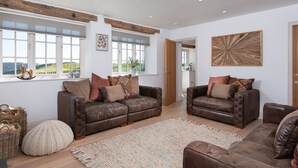 A spacious living room with leather sofas, a large woven rug, and a view of the outdoors through large windows. - Hawkrigg Farm (Ambleside)