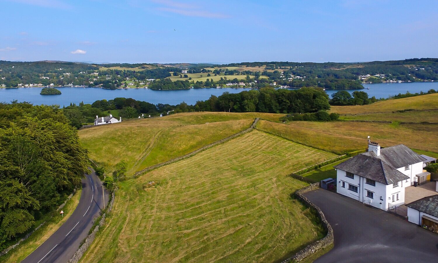 A rural landscape with a white house, a road, and a lake in the background.