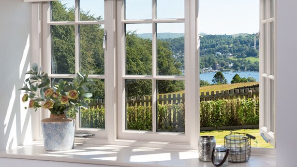 A room with a large window offering a view of a lake, greenery, and distant buildings. - Hawkrigg Farm (Ambleside)