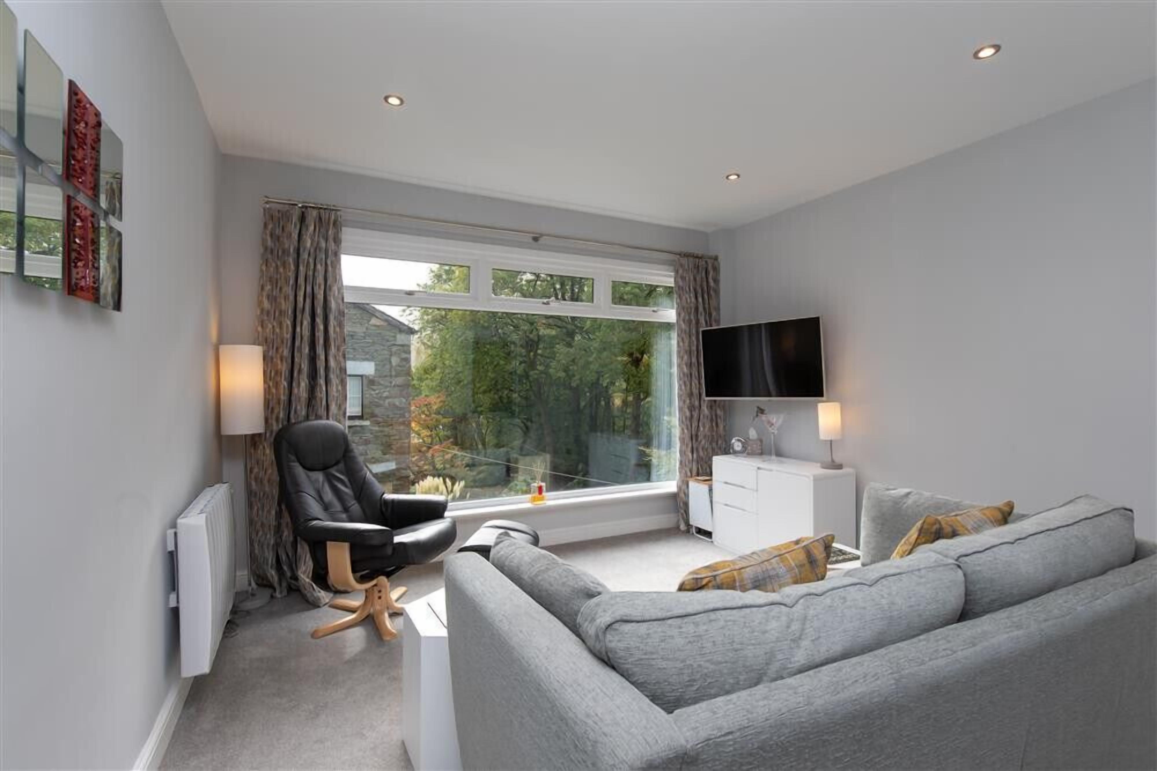 A modern living room with a grey sofa, a black chair, a TV, and a window with curtains.